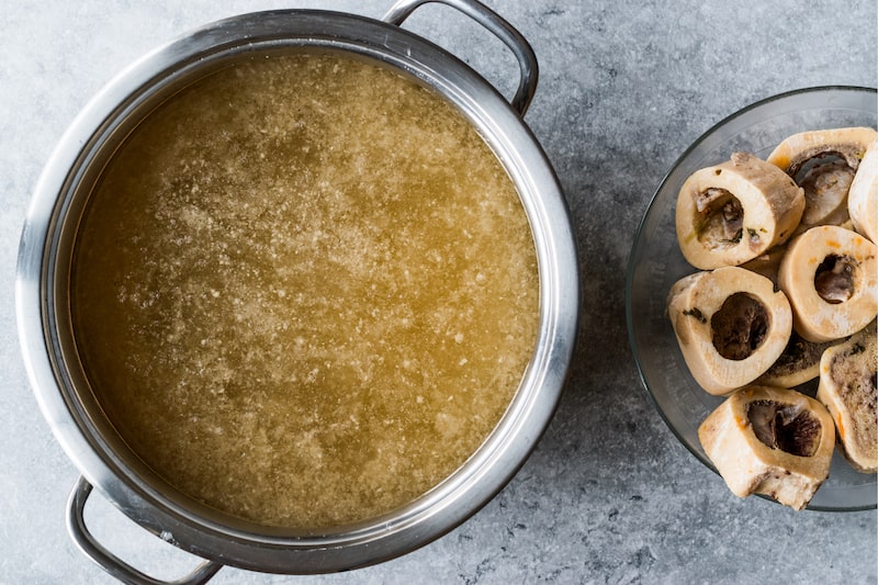 Simmering pot of bone broth next to chunks on animal bone