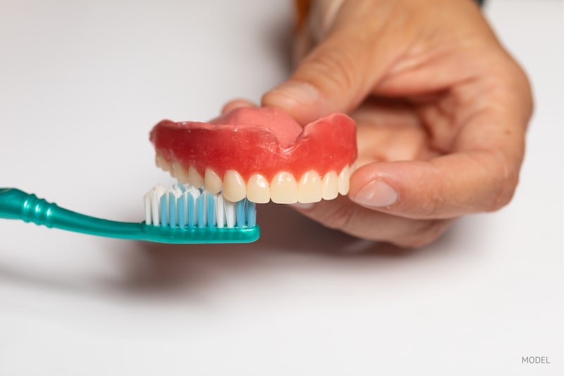 Close-up image of a person brushing their dentures with a toothbrush.